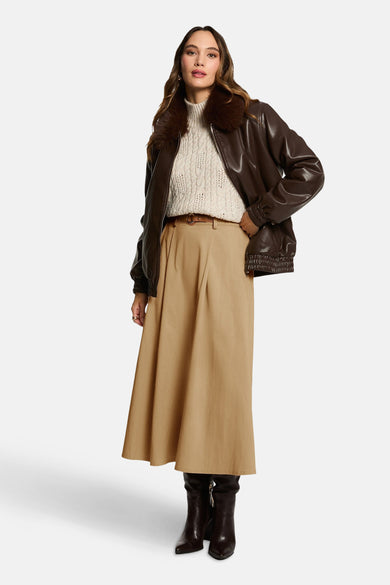 Manteau court brun de Morgan De Toi, avec col en fourrure imitée, associé à un pull tricoté, une longue jupe et des bottes.