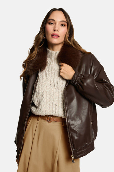 Manteau court brun de Morgan De Toi avec un col en fourrure, porté avec une chemise beige et un pantalon.