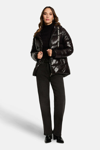 Manteau court noir de Morgan De Toi, avec une finition brillante et porté avec un gilet noir et des jeans.