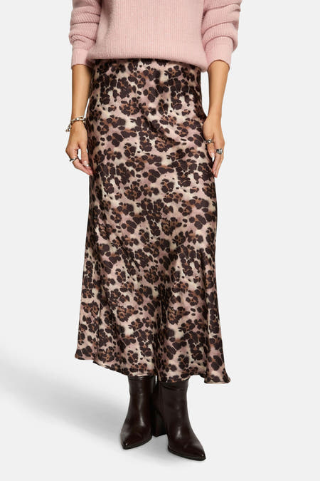 Longue jupe de Morgan De Toi, avec imprimé léopard multicolore, portée avec des bottes brunes et un pull rose.