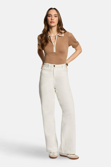 Polo beige à manches courtes de Morgan De Toi, avec des détails blancs et porté avec un pantalon blanc.