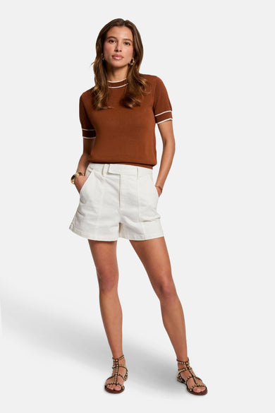 Pull marron avec col rond de Morgan de Toi, avec des bordures blanches, associé à un short blanc et des sandales avec des strass.
