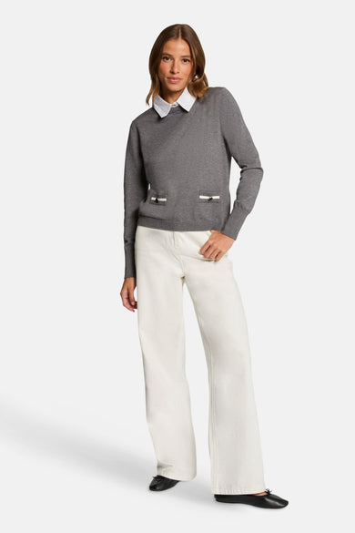 Sweat-shirt gris à col montant de Morgan De Toi, avec des poches élégantes et porté avec une blouse blanche et un pantalon blanc large.