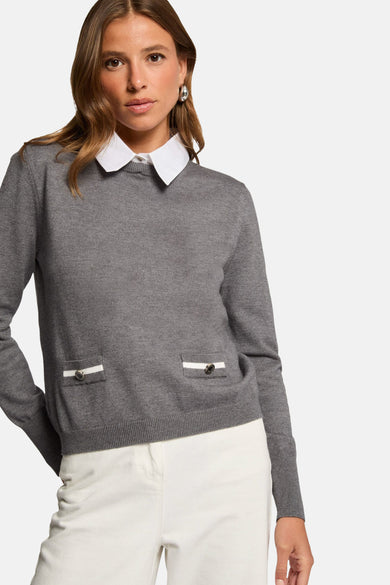 Pull à col rabattu gris de Morgan De Toi, avec des poches décoratives et porté avec un chemise blanc et un pantalon blanc.