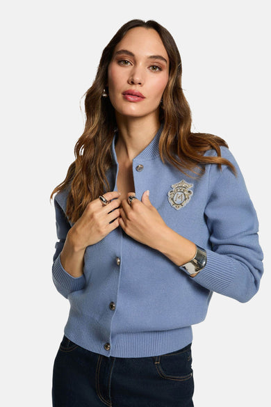 Gilet bleu de Morgan De Toi avec des boutons décoratifs, porté avec un pantalon foncé et des bijoux argentés.