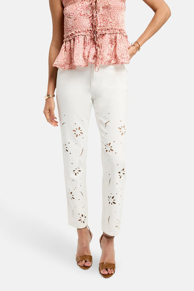 Pantalon blanc de Morgan De Toi, avec des détails floraux et associé à une chemise rose et à des baskets brunes.