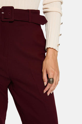Pantalon de Bordeaux de Morgan De Toi, avec ceinture et grande boucle, porté avec un pull beige à des détails dorés.