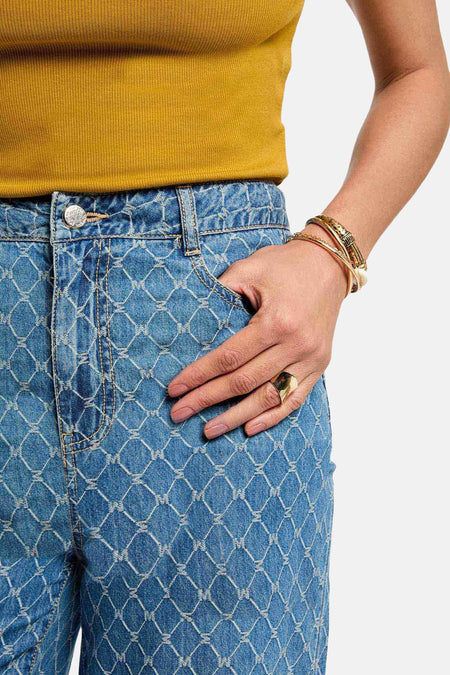 Jean bleu de Morgan De Toi, avec motif de lunettes, bague d'or et bracelets, main dans la poche.
