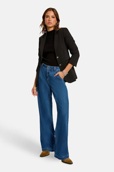 Blazer noir de Morgan De Toi, porté sur un gilet noir et des jeans bleus délavés, avec des chaussures marron.
