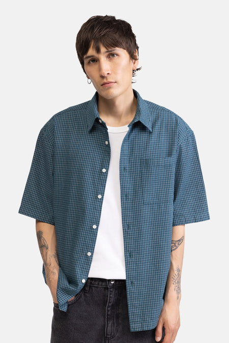 Chemise verte à fines rayures et manches courtes de REDEFINED REBEL, portée ouverte sur un t-shirt blanc par un homme tatoué.