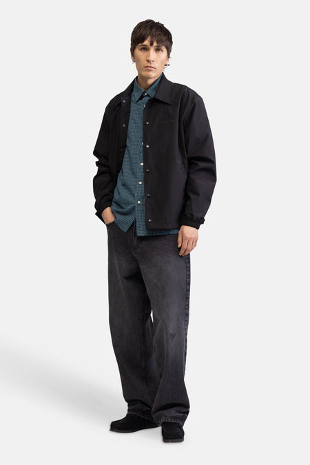 Chemise à manches courtes à carreaux verts de REDEFINED REBEL, avec de petits carreaux, portée sous une veste noire.