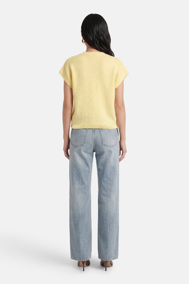 Gilet jaune de Terra di Siena, à manches courtes et à texture finement tricotée, combiné avec un jean bleu et des talons marron, vu de dos.