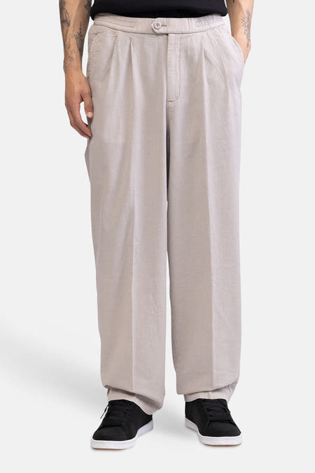 Vue de côté d'un pantalon écru de REDEFINED REBEL, ample, avec une texture subtile et une poche arrière, porté avec des baskets noires.