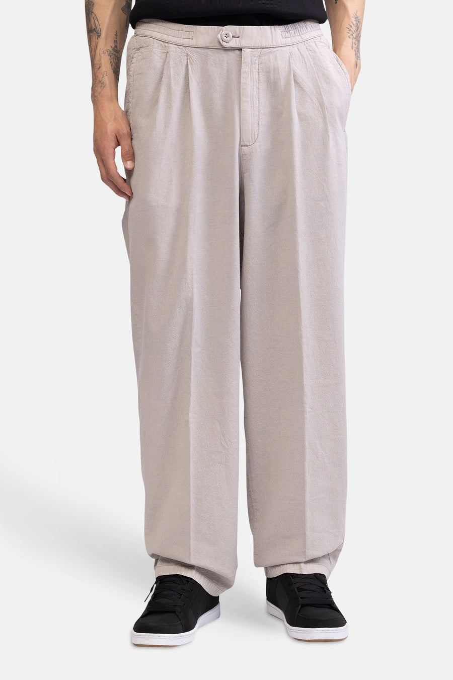 Vue de côté d'un pantalon écru de REDEFINED REBEL, ample, avec une texture subtile et une poche arrière, porté avec des baskets noires.