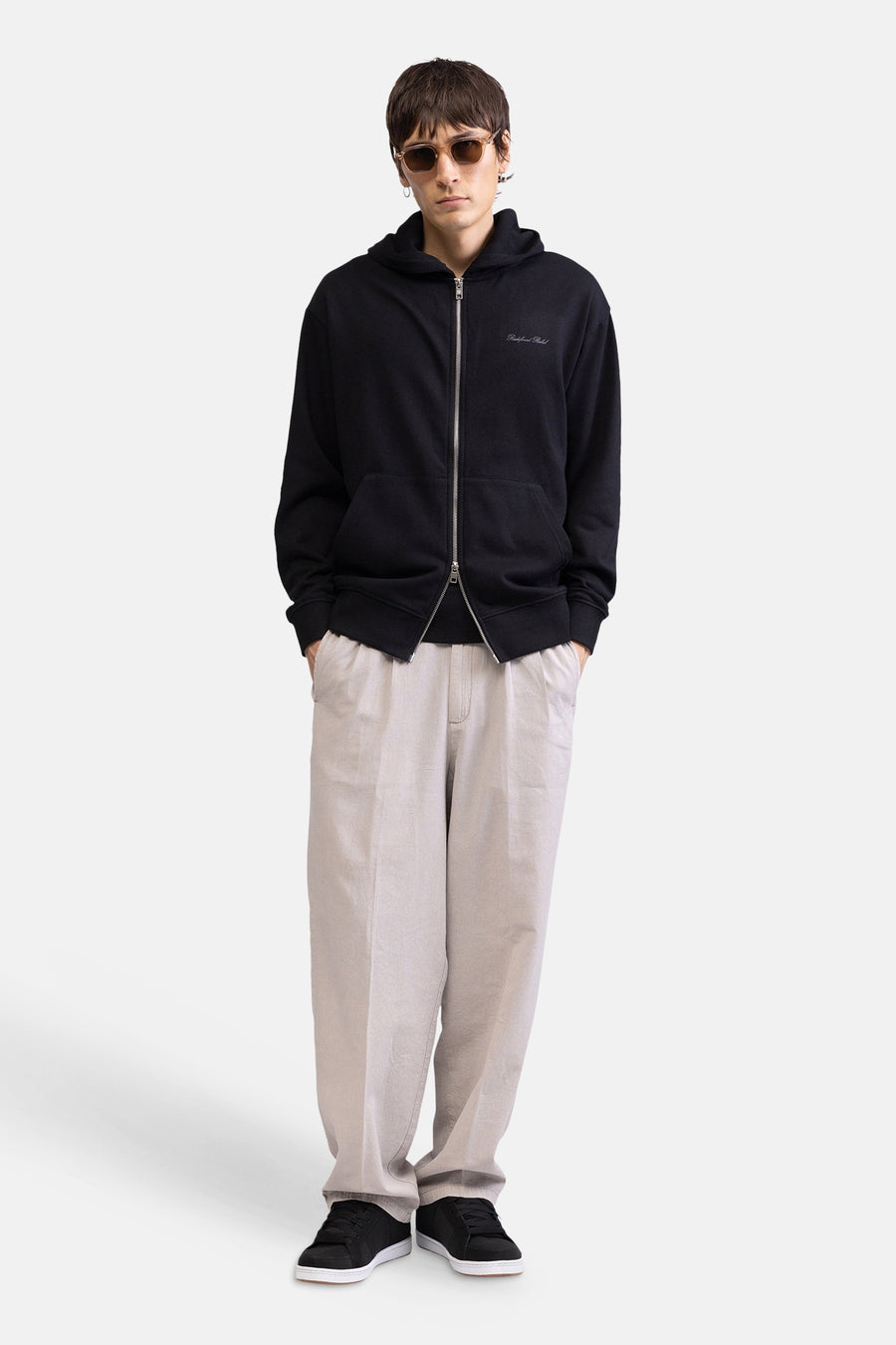 Pantalon écru de REDEFINED REBEL, coupe ample, porté par un homme avec un sweat à capuche noir et des baskets.