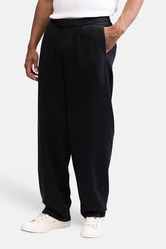 Pantalon noir de REDEFINED REBEL avec coupe ample, taille élastique et poche latérale, porté avec un t-shirt blanc et des baskets beiges.