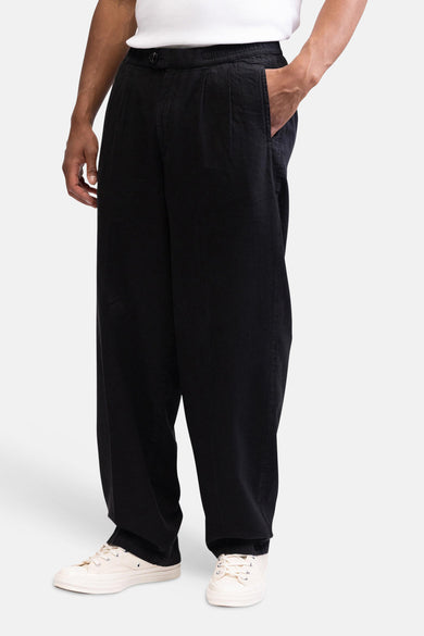 Pantalon noir de REDEFINED REBEL avec coupe ample, taille élastique et poche latérale, porté avec un t-shirt blanc et des baskets beiges.
