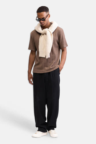 Pantalon noir de REDEFINED REBEL, avec une texture subtile et une coupe décontractée, porté par un homme avec une chemise marron et des baskets blanches.