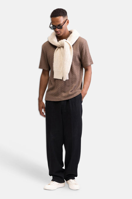 Pantalon noir de REDEFINED REBEL, avec une texture subtile et une coupe décontractée, porté par un homme avec une chemise marron et des baskets blanches.