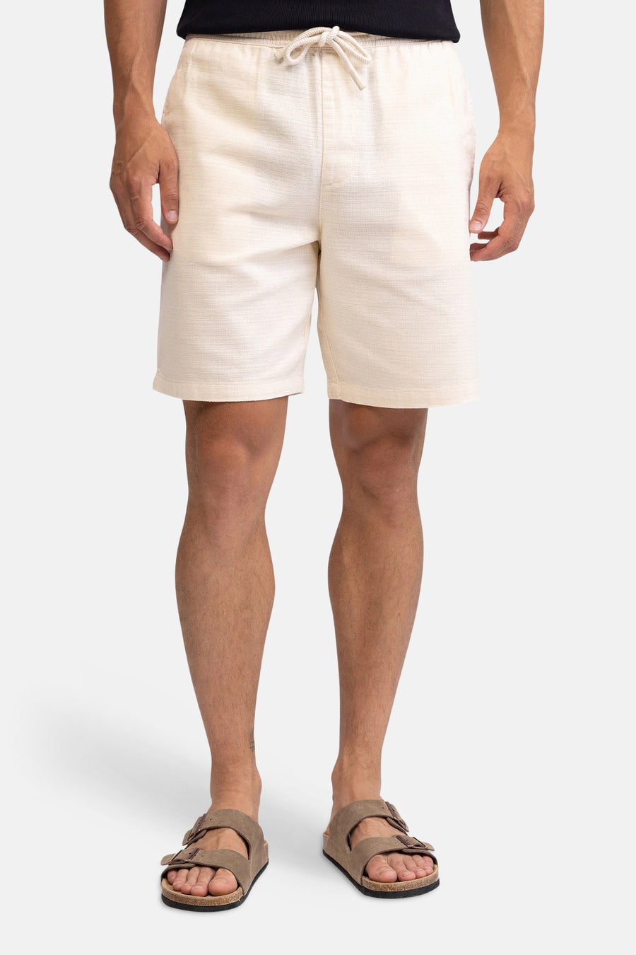 Short en lin d'aspect écru de REDEFINED REBEL, vu de dos, avec taille élastique et poches passepoilées, porté par un homme avec des sandales marron.