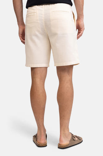 Ecru linnenlook short van REDEFINED REBEL, gezien van achteren, met elastische tailleband en paspelzakken, gedragen door een man met bruine sandalen.