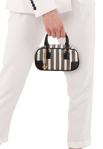 Sac à bandoulière noir Morgan De Toi avec motif à rayures et breloque "M" dorée, porté avec un pantalon blanc et un blazer.