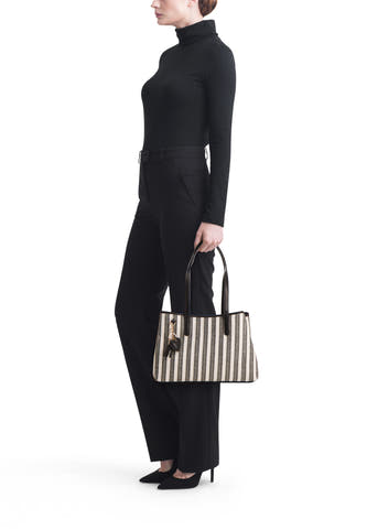 Sac à bandoulière noir de Morgan De Toi, avec des rayures verticales et un porte-clés, porté avec un col roulé noir et un pantalon noir.