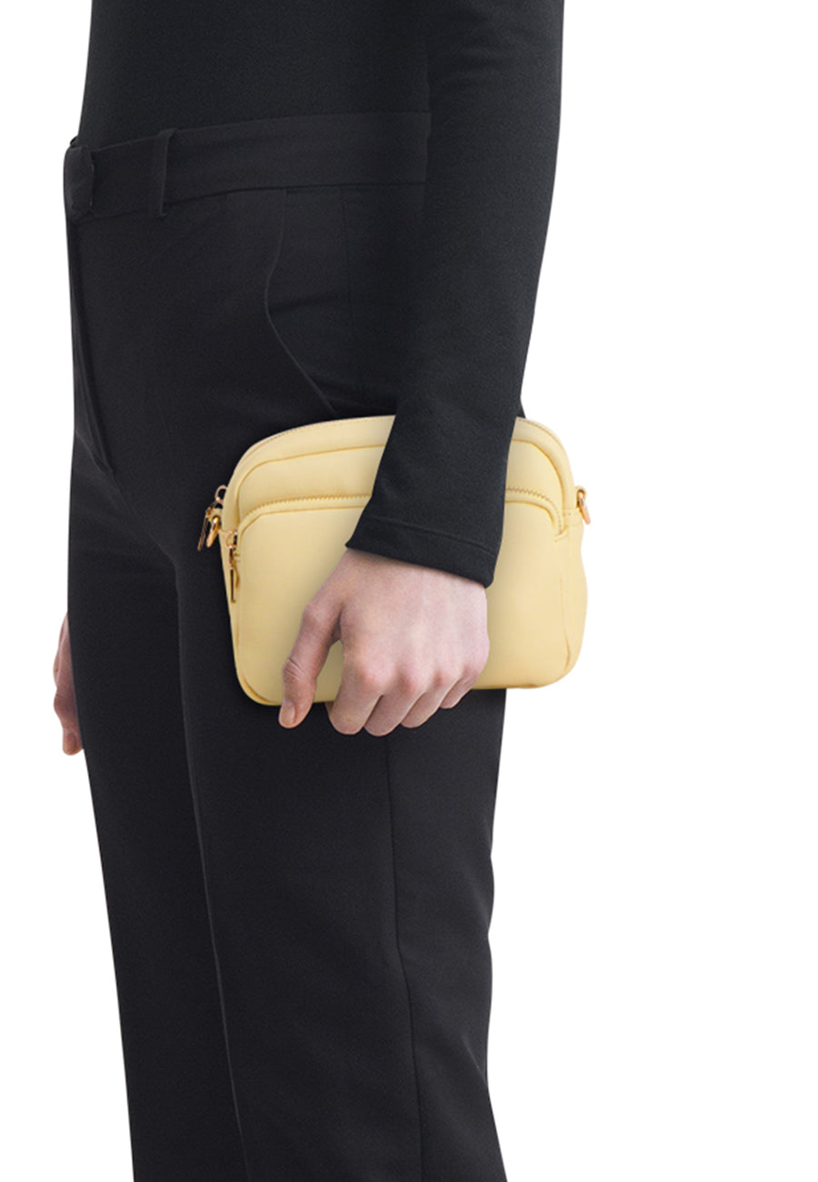 Sac à bandoulière jaune de Morgan De Toi, tenu par une personne vêtue de noir, avec des fermetures éclair dorées et une surface légèrement texturée.