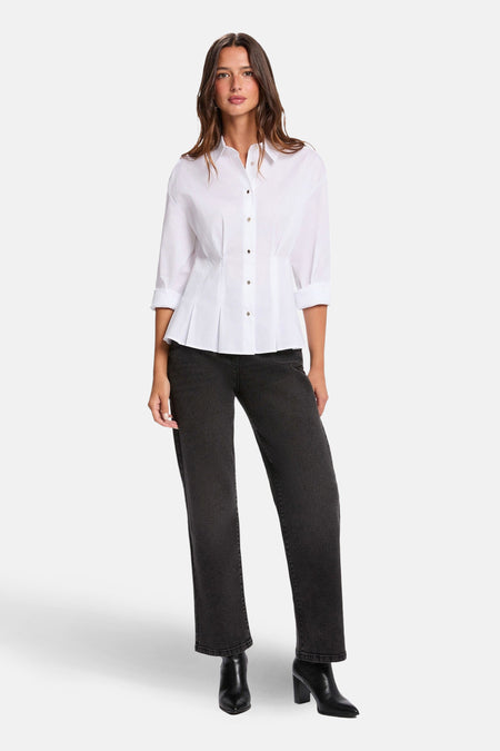 Vrouw staat in witte blouse, zwarte jeans en zwarte laarsjes.