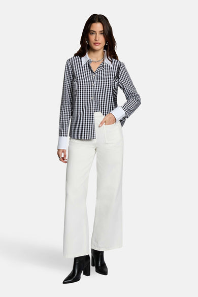Chemise à carreaux noirs et blancs à manches longues de Morgan De Toi, avec col et poignets blancs, combinée avec un pantalon blanc et des bottes noires.