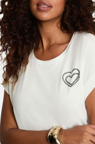 T-shirt blanc à manches courtes de Morgan De Toi, avec un imprimé de cœurs en strass, porté avec un bracelet d'or.