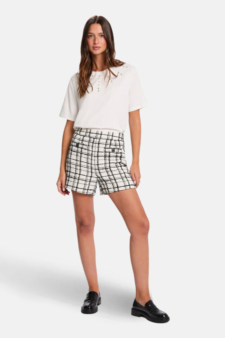 Vrouw draagt wit T-shirt en geruite shorts, staand.