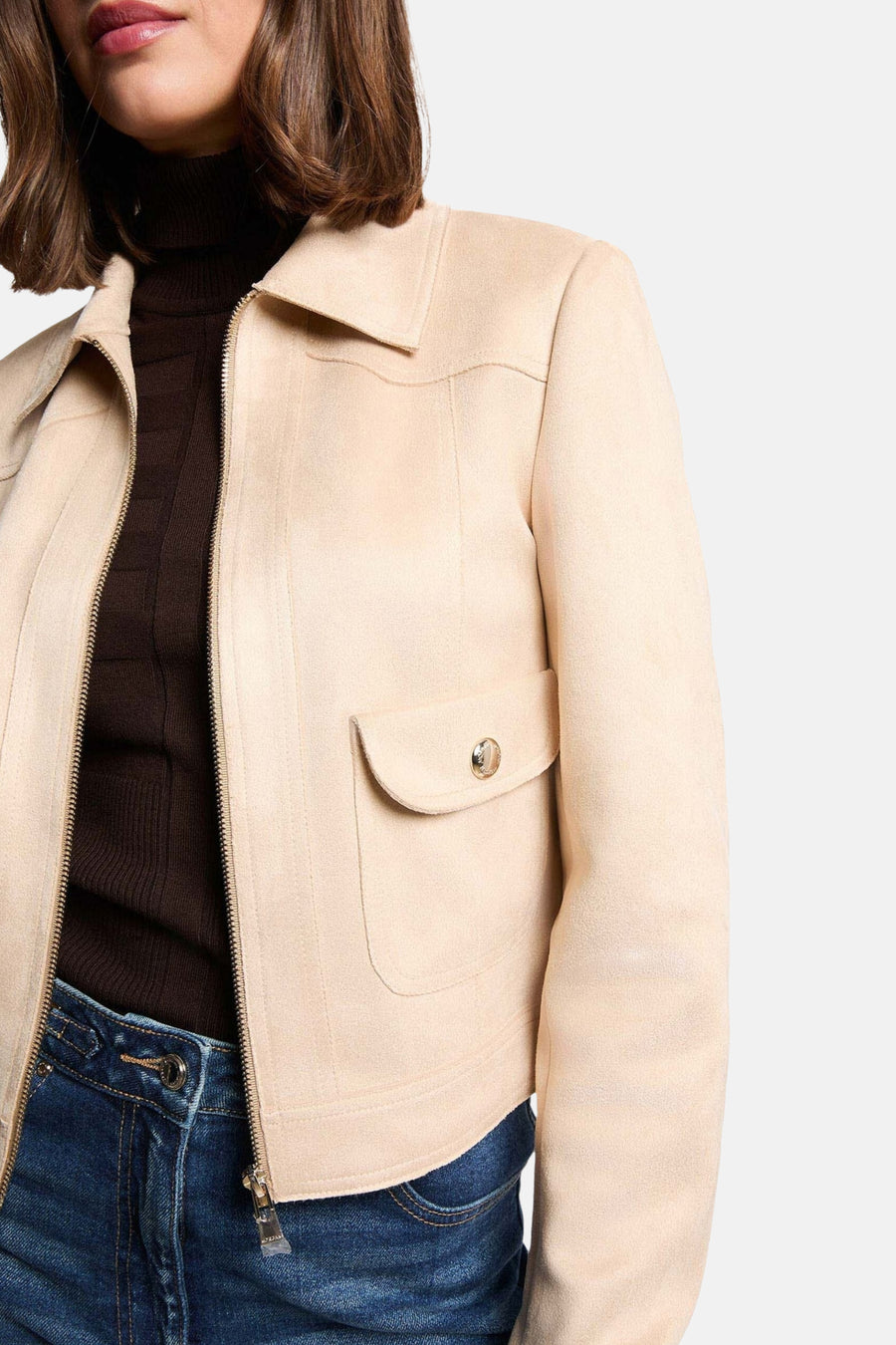 Crèmekleurige jas met bruine coltrui en blauwe spijkerbroek.