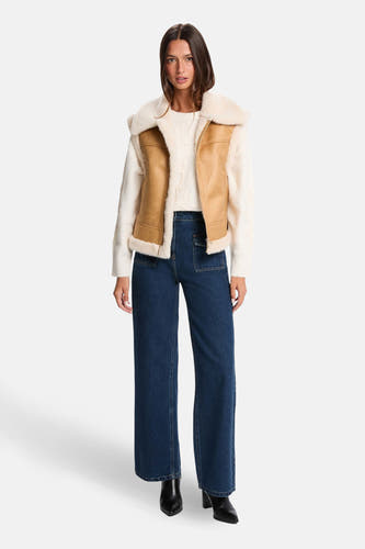 Cognackleurige bodywarmer van Morgan De Toi, met crèmekleurige voering gedragen over een gebreide trui en donkerblauwe broek.
