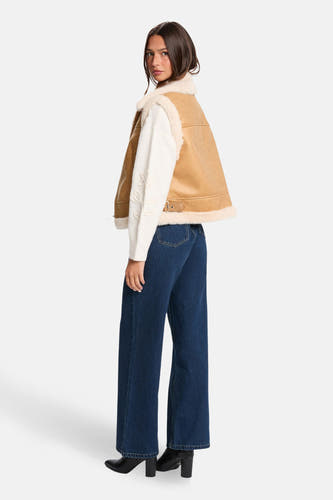 Cognackleurige bodywarmer van Morgan De Toi, met faux bontrand, gedragen over een witte trui en donkerblauwe jeans.