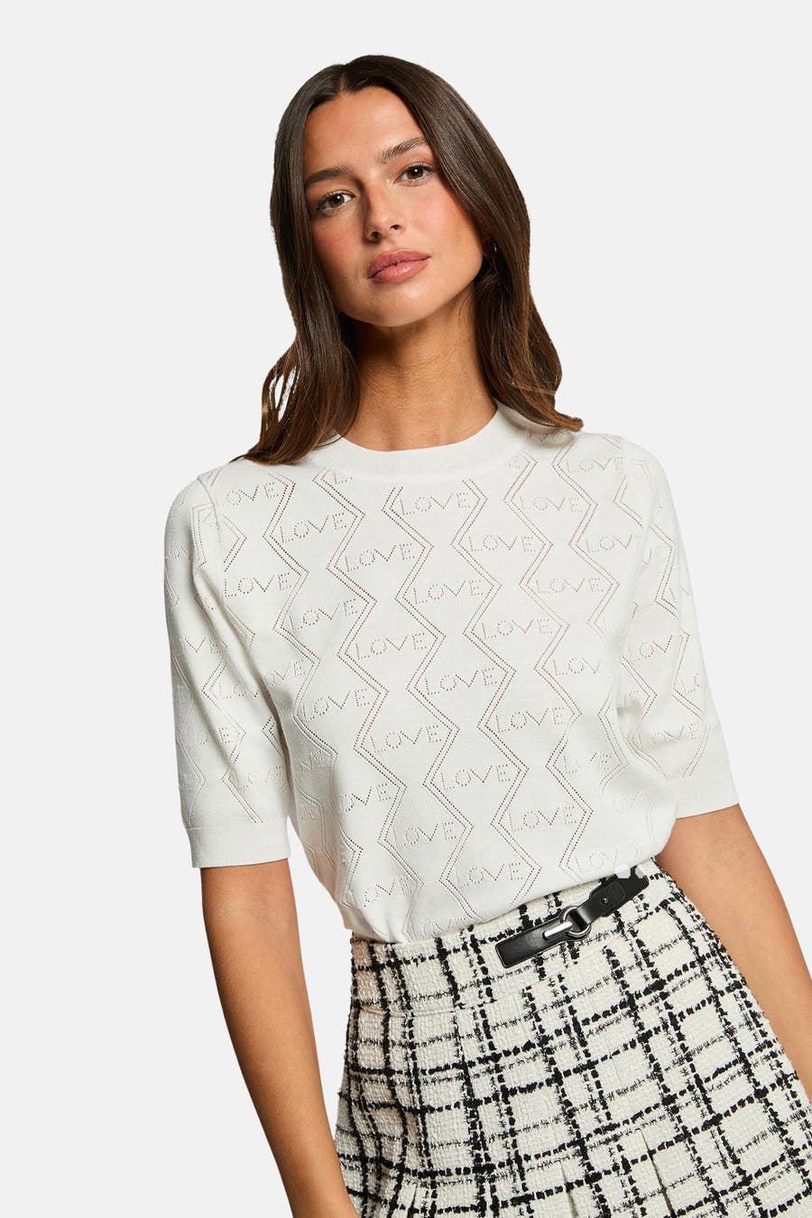 Pull-over blanc avec col rond de Morgan De Toi, avec un motif ajouré ouvert port le mot 'Love' et une jupe rayée noire et blanche.