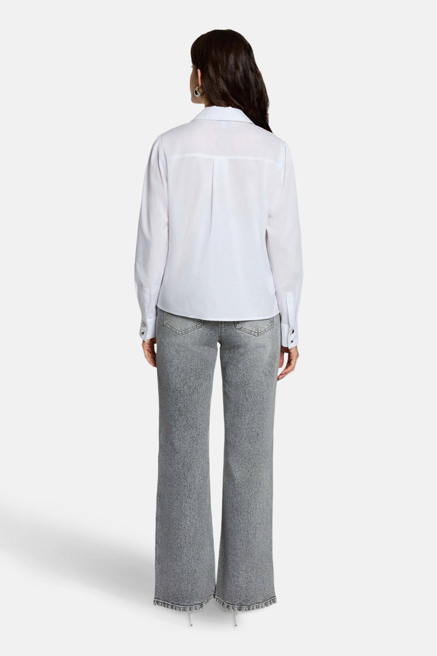 Achterkant van een vrouw in een wit overhemd en grijze jeans.