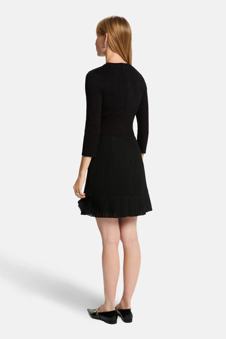 Zwarte jurk met plooirok, staande pose.