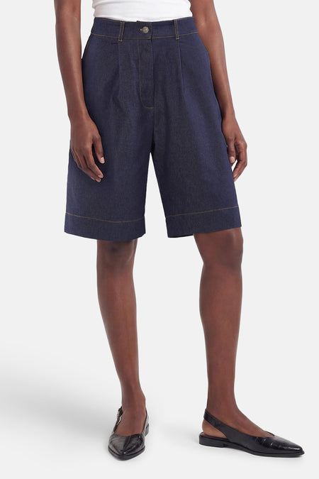 Bermuda en denim bleu marine de Morgan De Toi avec plis, surpiqûres jaune or et ourlet retroussé, porté avec un haut blanc et des mocassins noirs.