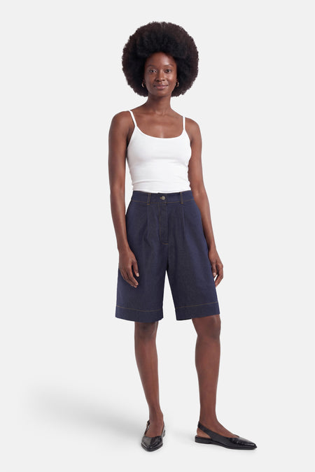 Bermuda en denim bleu marine de Morgan De Toi avec plis et surpiqûres jaunes, porté avec un top à fines bretelles blanc et des slingbacks noirs.