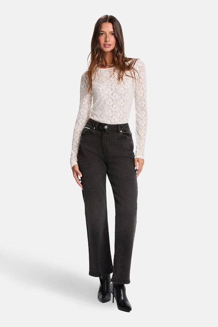 Vrouw in witte kanten top, zwarte jeans en zwarte laarsjes, staand.