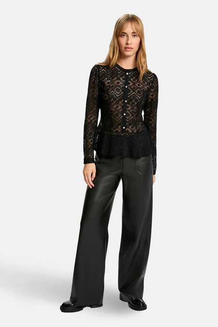 Vrouw in zwarte kanten blouse en zwarte leren broek.