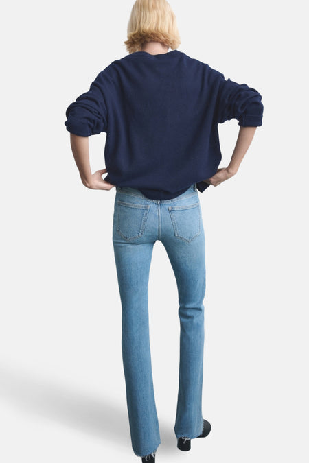 Achterkant van een vrouw in een marineblauwe trui en lichtblauwe jeans.