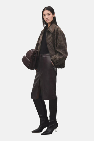 T-shirt noir à manches longues de MANGO, col montant et stylisé avec une veste à carreaux marron et une jupe en cuir marron foncé.