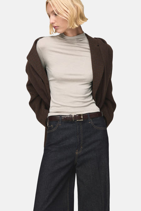 T-shirt beige à manches longues de MANGO, vu de dos avec un pantalon foncé et une ceinture marron.