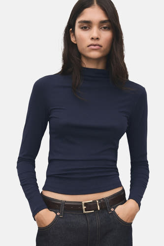 T-shirt bleu à manches longues de MANGO, vu par derrière, associé à un pantalon foncé et une ceinture marron.