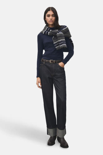 T-shirt bleu à manches longues de MANGO, associé à un foulard rayé porté négligemment sur les épaules, combiné avec des jeans foncés et une ceinture marron.