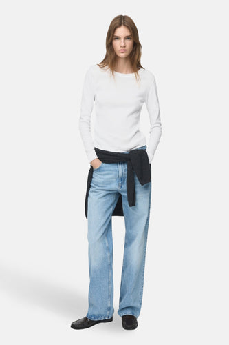 T-shirt blanc à manches longues de MANGO, porté avec un pull sombre autour de la taille et des jeans larges.