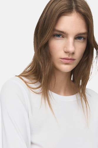 T-shirt blanc à manches longues de MANGO, porté par une femme aux cheveux détachés.