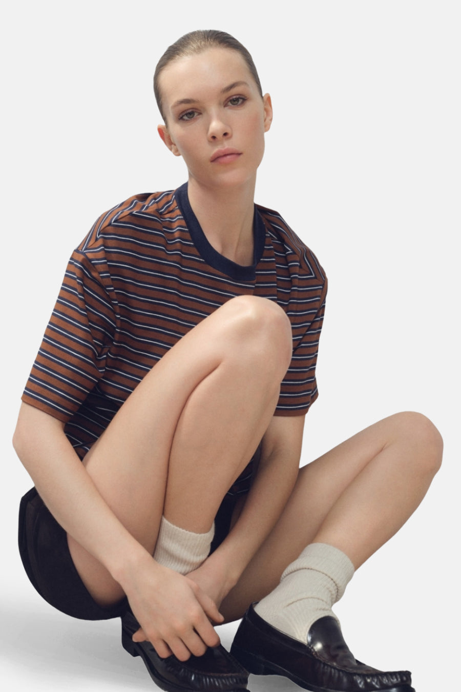 T-shirt multicolore à manches courtes de MANGO, avec des rayures horizontales, porté avec des shorts noirs, des chaussettes blanches et des chaussures noires.